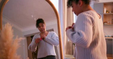 Genç bir kadın, aynaya bakarken meme kanseri farkındalığını desteklemek için pembe kurdele takıyor.