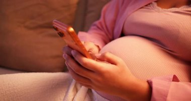 Müstakbel annenin kanepeye uzandığı ve sıcak bir odada akıllı telefonunu kullandığı yakın plan.