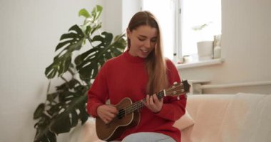 Neşeli bayan müzisyen, rahat bir oturma odasında telli çalgısıyla pratik yapıyor.