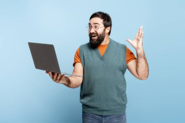 Mutlu sakallı adam online başarısını kutluyor, sürpriz ve heyecanla dizüstü bilgisayara bakıyor.