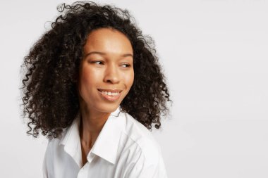 Siyah kıvırcık saçlı, gülümseyen ve yüzünü çeviren bir kadın, gerçek mutluluk ve otantik bir ruh hali sergiliyor.