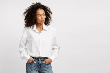 Woman standing with hands in pockets, looking away, reflecting on thoughts on a white background