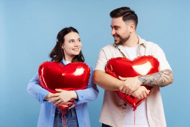 Mavi arka planda izole edilmiş kırmızı balonları tutan mutlu çiftin portresi. Sevgililer Günü konsepti