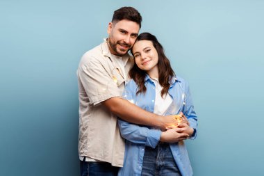 Mutlu bir çiftin portresi, sarılan güzel bir kadın mavi arka planda izole edilmiş kameraya bakıyor. İlişki, Sevgililer Günü konsepti