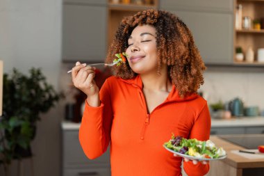Kadın gözlerini kapatıyor, sağlıklı bir yaşam tarzı için taze yeşil salata kokluyor ve yiyor.