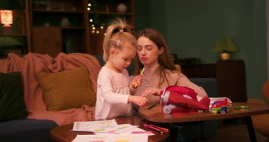 Sevimli kızına evde renkli kalemlerle resim yapmayı öğreten şefkatli bir anne.