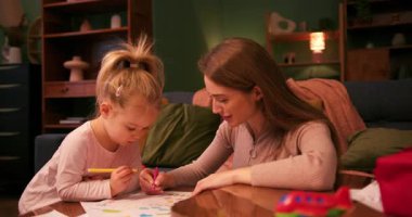 Küçük kızına resim yapmayı öğreten genç bir kadın, sıcak bir oturma odasında birlikte vakit geçiriyor.