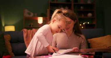 Sevgi dolu bir anne, evde yaratıcı bir gece boyunca küçük kızına makasla kağıt kesmesinde yardım ediyor.