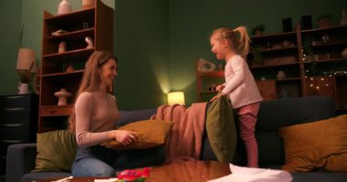 Neşeli genç anne ve tatlı küçük kızı akşam evde yastık savaşı yapıyorlar.