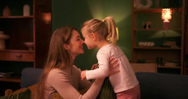 Küçük mutlu kız annesine bir yastık veriyor. Bu arada onlar da rahat bir oturma odasında kanepede oynuyorlar.