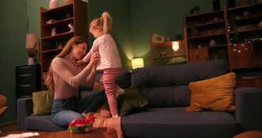 Mutlu küçük kız kanepede zıplayıp sevgili annesinin kucağına atlıyor.