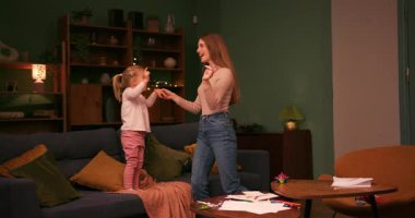 Sevgi dolu bir anne, oturma odasındaki kanepede zıplayıp küçük kızıyla eğleniyor.