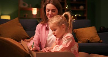 Şefkatli anne, sevimli küçük kızına sıcak bir odada otururken nasıl çizim yapacağını öğretiyor.