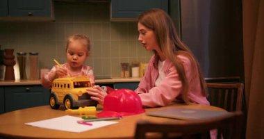 Genç bir kadın ve küçük tatlı kızı mutfak masasında oyuncaklarla oynuyorlar.