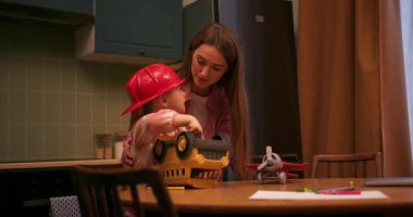 Mutlu anne ve kız, akşam vakti mutfak masasında oyuncak bir kamyon ve tornavida ile oynuyorlar.