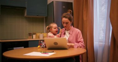 Uzaktan kumandayla çalışan serbest çalışan genç bir anne. Yanında oynak çocuğu oturuyor.