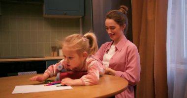 Genç anne, yeni yürümeye başlayan kızıyla birlikte mutfakta resim çizip oyun oynuyor.