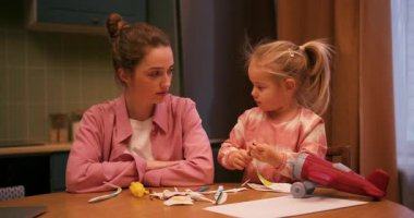 Stresli genç bir kadın, kızı mutfak masasında oyuncaklarla oynarken yorgun hissediyor.