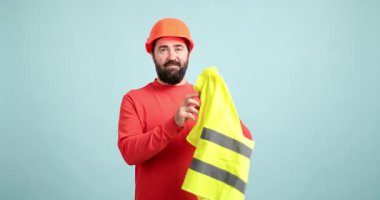 Sakallı erkek işçi güvenlik yeleği giyer ve kollarını düz bir zemine geçirir.