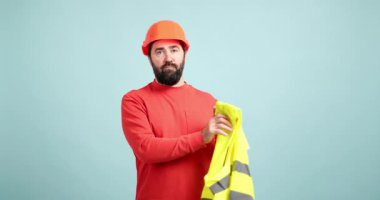 Erkek mühendis sıkı bir şapka ve yüksek görüş mesafesi olan bir yelek giyerek işe hazırlanıyor.