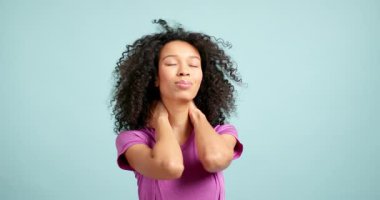 Boynunda ağrı hisseden genç bir kadın, mavi arka planda elleriyle ağrıyan kaslara masaj yapar.