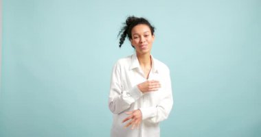 Beyaz tişörtlü neşeli genç kadın dans ediyor ve açık mavi arka planda eğleniyor.