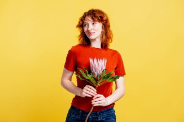 Kızıl saçlı ve çilli bir kadın gülümserken çiçek açıyor.