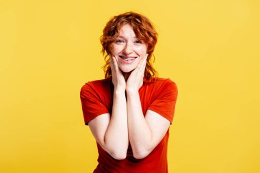 Kıvırcık kızıl saçlı ve telleri geniş gülümseyen, olumlu duyguları olan mutlu genç bir kadın.