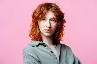 Tarafsız ve düşünceli duygularını ifade eden belirgin kızıl saçlı ve çilli genç bir kadın.