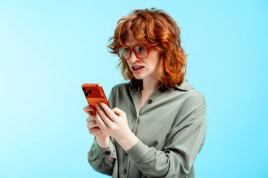 Kızıl saçlı kadın endişeli bir ifadeyle akıllı telefona bakıyor, hayal kırıklığı yaşıyor ve şok geçiriyor.