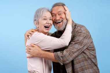 Olumlu, gülümseyen yaşlı bir çiftin portresi, mavi arka planda izole edilmiş güzel bir kadını kucaklayan yakışıklı bir adam. Aşk, ilişki kavramı