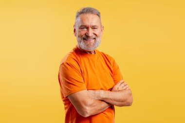 Sarı arka planda izole edilmiş kameraya bakarak kollarını çapraz bağlamış turuncu tişört giyen mutlu, pozitif bir son sınıf öğrencisi. Reklam kavramı