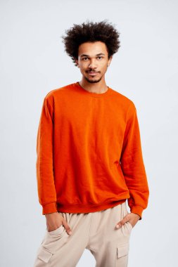 Genç adam dikilip kameraya bakıyor. Yüzünde dostane bir ifade var.