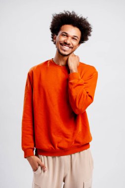 Genç adam poz veriyor, açık gri arka planda mutluluk ve olumlu duygular gösteriyor.