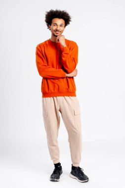 Genç adam ayakta, kıvırcık saçlı, günlük giysiler, düşünceli eller çenede, stüdyo portresi