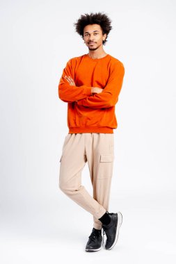 Afro saçlı genç adam ciddi bir ifadeyle ayakta duruyor, rahat bir stil ve bireysellik sunuyor.