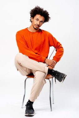 Stüdyoda oturan kendinden emin genç siyahi adam, afro saç stili ile gündelik modellik yapıyor.