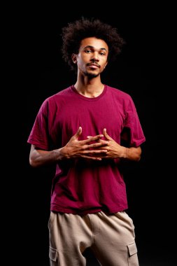 Kendinden emin genç siyah adam kameraya bakıyor, elleri göğsüne kenetlenmiş duruyor.