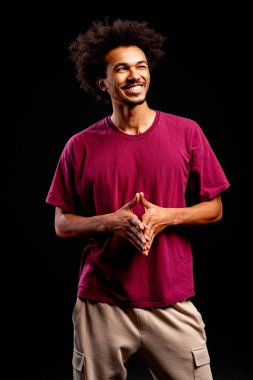 Siyah saçlı, gülümseyen ve ayakta duran, siyah arka planda mutlu görünen genç bir zenci.