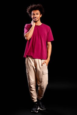 Kıvırcık saçlı ve gülümseyen genç bir adam siyah arka planda duruyor.