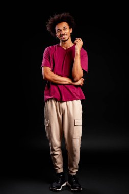 Ayakta duran, kendine güven ve mutluluk saçan, karanlık bir arka planda soyutlanmış genç adam.