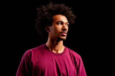 Afro saçlı, sıradan tişörtlü düşünceli Afro-Amerikan bir adam, yana bakıyor.