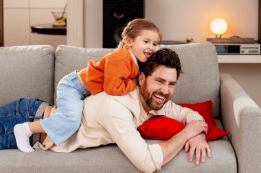 Baba ve kızı kanepede oynuyorlar, birlikte eğleniyorlar, evde ailece vakit geçiriyorlar.