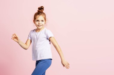 Genç kız gülümsüyor ve hareketlerini pembe bir stüdyonun arka planında ifade ediyor.