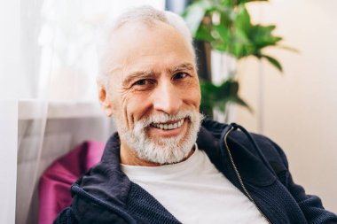 Gülümseyen mutlu, dişleri sırıtan, modern evde kameraya bakan yaşlı bir adamın portresi. Reklam kavramı