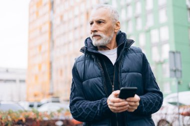 Ciddi, olgun bir adam cep telefonu kullanıyor. Cep telefonu uygulaması kullanıyor, sohbet ediyor, sokakta mesaj yazıyor ve fotokopi uzayına bakıyor. Çevrimiçi teknoloji kavramı