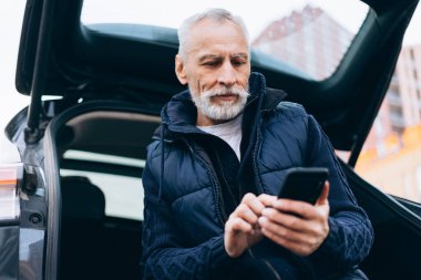 Elinde cep telefonu mesajı tutan yakışıklı bir adam açık havada arabada oturuyor. Çevrimiçi teknoloji kavramı