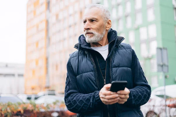 Ciddi, olgun bir adam cep telefonu kullanıyor. Cep telefonu uygulaması kullanıyor, sohbet ediyor, sokakta mesaj yazıyor ve fotokopi uzayına bakıyor. Çevrimiçi teknoloji kavramı
