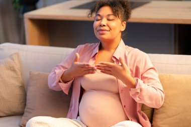 Hamile, güzel, Afro-Amerikan bir kadın. Kapalı gözlerle nefes alıyor. Evdeki rahat oturma odasında rahat bir koltukta oturuyor. Uyum kavramı