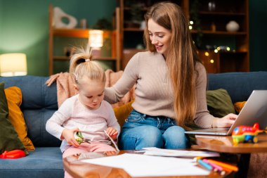 Anne ve kızı evde aynı anda birden fazla iş yapıyor. Kadın çalışıyor ve çocuk makasla yaratıyor